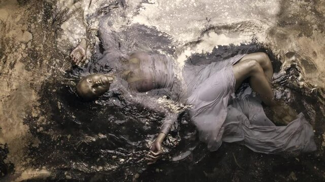 abstract shot of young woman lying in water with golden shiny paint, colored skin of sexy model