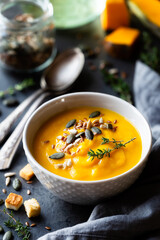 Pumpkin cream soup in a bowl garnished with mixed seeds and fresh thyme against dark rustic background