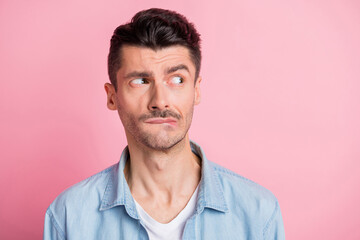 Photo of displeased brunette young man look empty space bite teeth lips isolated on pastel pink color background