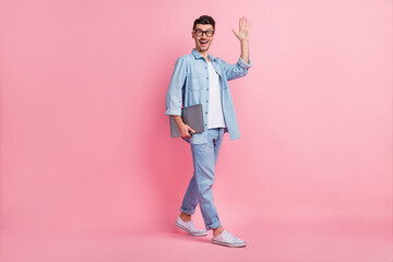 Full length body size view of nice cheerful guy carrying laptop waving hello isolated over pink pastel color background © deagreez