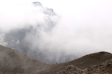 Fototapeta na wymiar Mountain range in the clouds. Two people are walking along the ridge. Caucasus, Russia