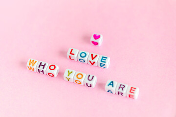 Phrase "Love who you are" made out of colorful beads on pastel pink background