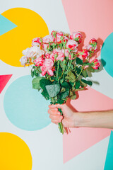 Spring rose flower bouquet in one hand on colorful pop art background. Minimal modern creative Valentines or woman's day concept.