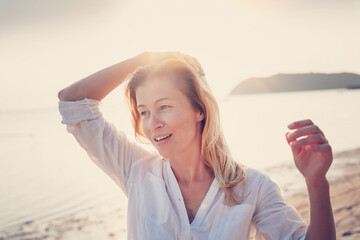 Beautiful happy adult blonde woman on the beach in sunlight, calm face close up