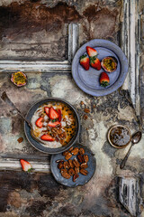 oatmeal with fresh berries, nuts and passionfruit sauce in blue bawl on shabby beige background, healthy breakfast concept