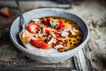 oatmeal with fresh berries, nuts and passionfruit sauce in blue bawl on shabby beige background, healthy breakfast concept
