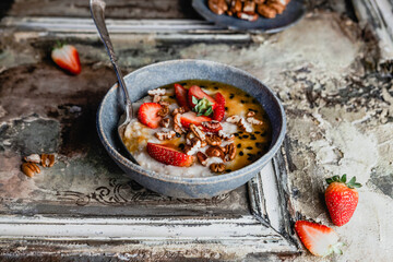 oatmeal with fresh berries, nuts and passionfruit sauce in blue bawl on shabby beige background, healthy breakfast concept