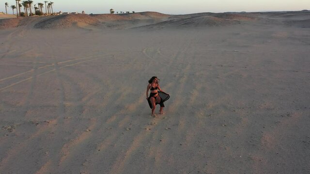 Aerial 360 shot of bellydancer dancing in desert at sunset