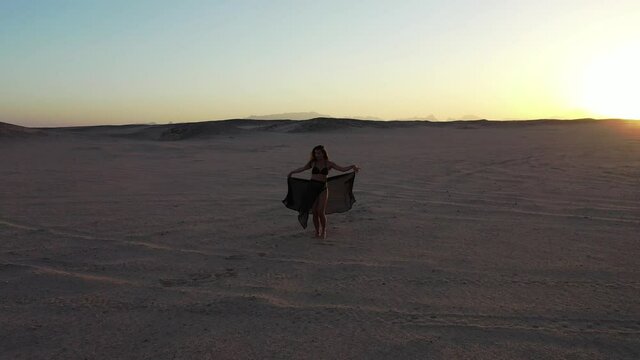 Aerial drone pull in shot of bellydancer dancing in desert sunset