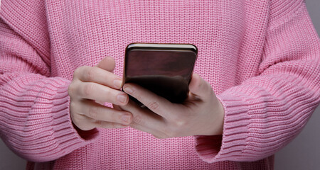 hands a girl in a pink sweater holding a black smartphone.