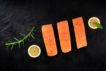 Salmon with lemons and herbs, overhead flat lay shot on a black background with a place for text