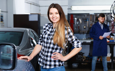 Obraz na płótnie Canvas Glad pleasant woman client is satisfied of repair of her car in spring in workshop.
