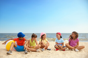 Group of children sitting on sand at sea beach. Summer camp
