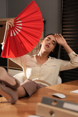 Woman with hand fan suffering from heat at home. Summer season © New Africa