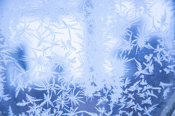 Snowflakes on the glass in winter. Frozen window. Frost on the glass of the window. Winter morning outside the window. Snowy frosty pattern on a glass surface. Background.