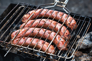 cooking sausages on the grill in the barbecue outdoors on a picnic