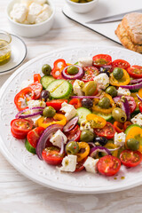 Fototapeta na wymiar Greek salad of fresh cucumber, tomato, sweet pepper, red onion, feta cheese and olives with olive oil dressing
