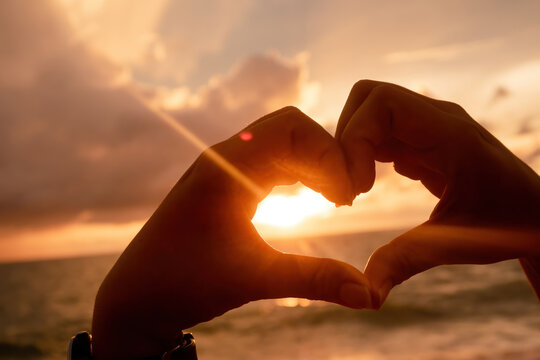 Concept of love The hand of the person making up the heart is raised for a picture with the sunset over the sea.