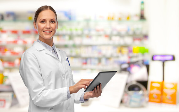 Medicine, Profession And Healthcare Concept - Happy Smiling Female Doctor Or Pharmacist In White Coat With Tablet Pc Computer Over Pharmacy Background