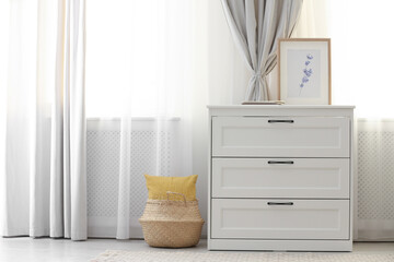 Chest of drawers near window with stylish curtains in living room. Interior design