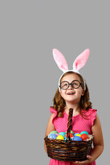 Happy easter. Cheerful little girl in a pink dress with polka dots holds a basket with eggs on a...