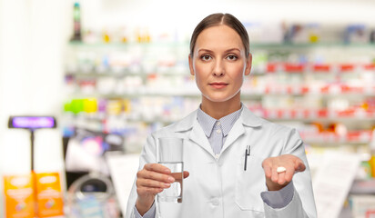 medicine, profession and healthcare concept - female doctor or pharmacist with pill and glass of water over pharmacy background
