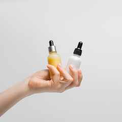 Several bottles of serum in a woman's hand on a light background. Vitamin C and hyaluronic acid.