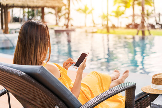 Young Woman Traveler Relaxing And Using A Mobile Phone By A Hotel Pool While Traveling For Summer Vacation