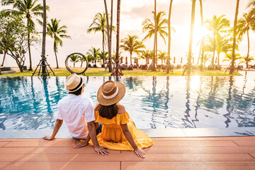 Young couple traveler relaxing and enjoying the sunset by a tropical resort pool while traveling for summer vacation - obrazy, fototapety, plakaty