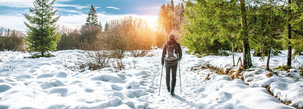 Popular winter outdoor activities. Male hiker hiking with backpack and Nordic walking poles in the snow.
