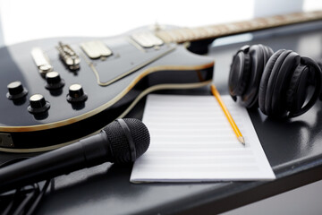 composing and music writing concept - close up of bass guitar with music book, microphone and headphones on black table