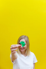 Shamrock in hand of young women in front of her face. Girl's face on yellow background. Selective focus.