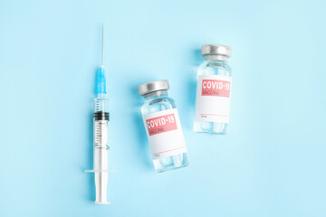 Vials with coronavirus vaccine and syringe on light blue background, flat lay