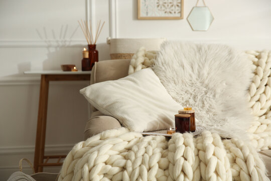 Candles on beige sofa with knitted blanket. Interior design