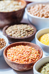 Raw red and green lentils in wooden bowls. Various dry cereals and legumes in white and wooden bowls, white marble background. Vegan protein concept.