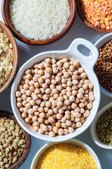 Raw chickpeas in white bowl. Various dry cereals and legumes in white and wooden bowls, white background. Vegan protein concept.