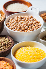 Raw chickpeas in a white bowl. Various dry cereals and legumes in white and wooden bowls, white marble background. Vegan protein concept.