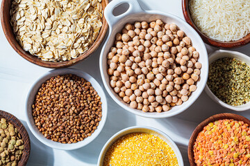 Raw chickpeas in a white bowl. Various dry cereals and legumes in white and wooden bowls, white marble background. Vegan protein concept.