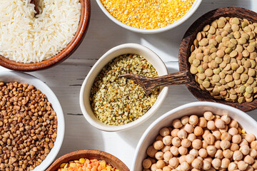 Raw hemp seeds in white bowl. Various dry cereals and legumes in white and wooden bowls, white wooden background. Vegan protein concept.