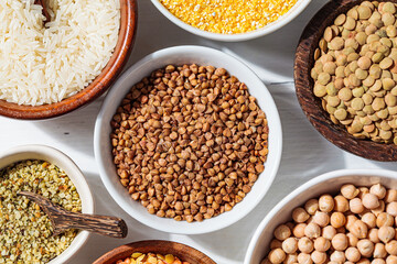 Raw buckwheat  in white bowl. Various dry cereals and legumes in white and wooden bowls, white wooden background. Vegan protein concept.