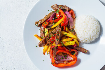 Peruvian cuisine concept. Lomo saltado - fried beef with peppers, onion, potato and rice on white plate, top view.
