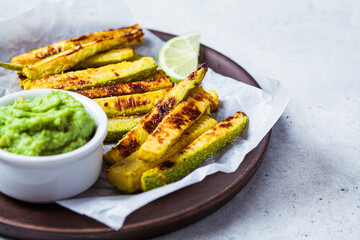 Zucchini fries with guacamole on wooden plate, gray background. Vegan food concept.
