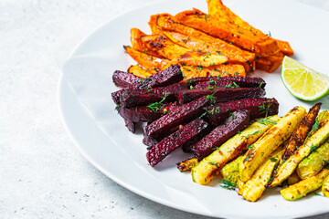 Baked slices of zucchini, sweet potato and beetroot on white plate, gray background. Vegan food concept.