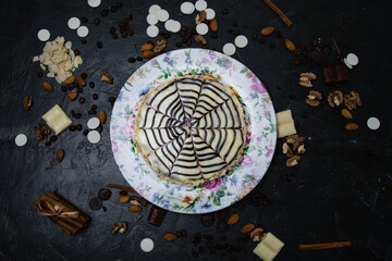 Cake with white and dark chocolate, cream, frosting, nuts, cinnamon and almonds view from the top, copy space, on a multi-colored plate, on a dark concrete background