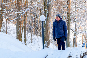 An elderly man of athletic build climbs the stairs in a winter landscape park in severe frost. Selective focus.