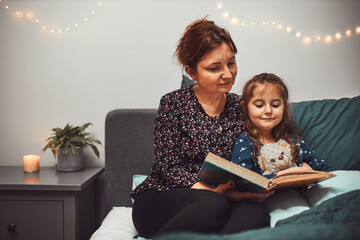 Mother reading book her daughter in bed before going to sleep. Reading stories before sleep. Bedtime stories for child