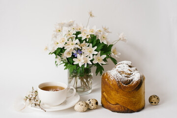Easter sweet bread, cake and eggs with white apple flowers and primroses, a cup of tea. Festive breakfast concept with copy space.