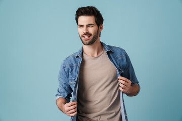 Young handsome unshaven man posing at camera over blue background