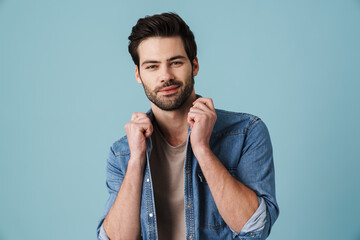 Young handsome unshaven man posing at camera over blue background