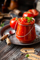 homemade red tomato sauce in glass jar on metal plate on wooden table with basil leaves